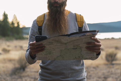 USA, Nordkalifornien, Nahaufnahme eines bärtigen Mannes, der bei einer Wanderung in der Nähe des Lassen Volcanic National Park ein Mobiltelefon und eine Karte benutzt, lizenzfreies Stockfoto