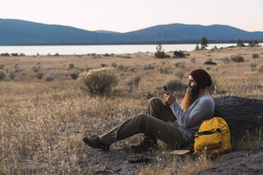 USA, Nordkalifornien, bärtiger junger Mann, der während einer Wanderpause in der Nähe des Lassen Volcanic National Park ein Mobiltelefon benutzt - KKAF02990