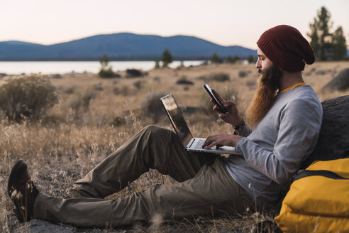 USA, North California, bearded young man using cell phone and laptop near Lassen Volcanic National Park - KKAF02991