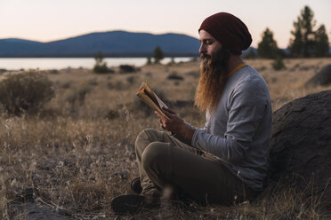 USA, North California, bearded young man reading a book near Lassen Volcanic National Park - KKAF02995