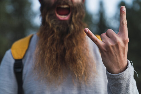 Close-up of screaming man with beard making horn sign - KKAF03004