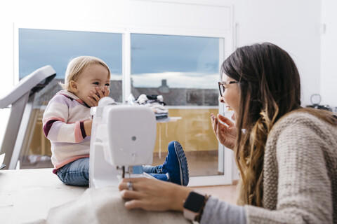 Glückliche Mutter mit kleiner Tochter zu Hause an der Nähmaschine, lizenzfreies Stockfoto