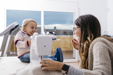 Happy mother with little daughter at home using sewing machine - JRFF02083