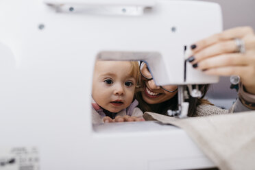 Kleine Tochter beobachtet ihre Mutter bei der Arbeit an der Nähmaschine zu Hause - JRFF02084