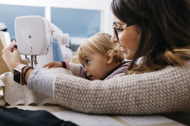 Happy mother with little daughter at home using sewing machine - JRFF02086