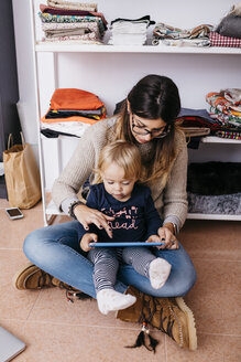 Mutter und kleine Tochter sitzen zu Hause auf dem Boden und benutzen ein Tablet - JRFF02098