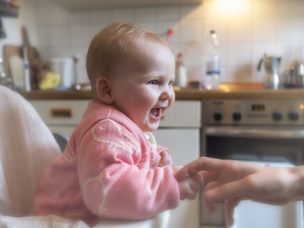 Happy baby girl in sitting in high chair in kitchen - LAF02184
