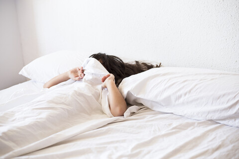 Mädchen liegt im Bett und bedeckt ihr Gesicht mit einer Decke, lizenzfreies Stockfoto