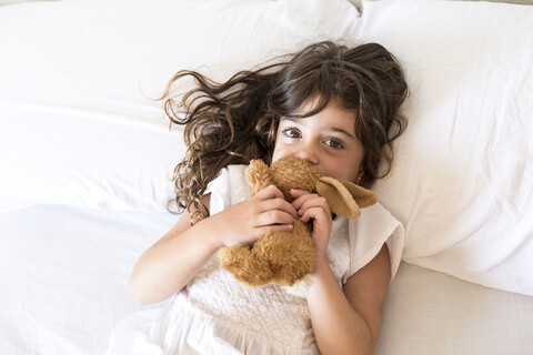 Little girl lying in bed with plush toy rabbit stock photo