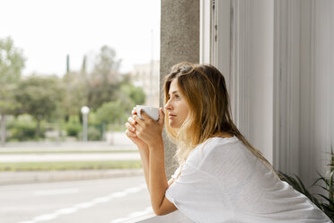Junge Frau am Fenster mit einer Tasse Kaffee in der Hand - ERRF00090