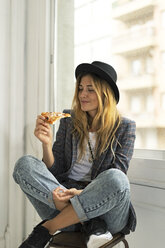 Junge Frau in einem Studio, die am Fenster eine Pizza isst - ERRF00096