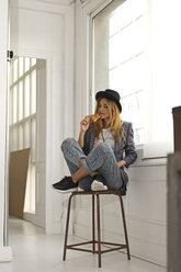 Junge Frau in einem Studio, die am Fenster eine Pizza isst - ERRF00098