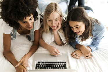 Drei Freundinnen liegen auf dem Bett und teilen sich einen Laptop - VABF01724