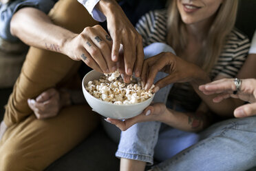 Nahaufnahme von Freunden, die auf der Couch sitzen und sich eine Schüssel Popcorn teilen - VABF01733