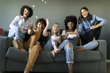 Exuberant friends sitting on couch throwing popcorn - VABF01735