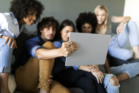 Freunde sitzen auf der Couch und schauen auf ein Tablet, lizenzfreies Stockfoto