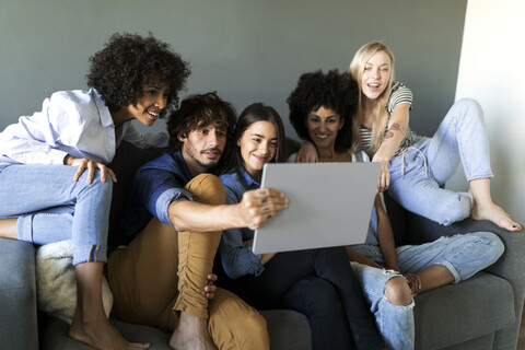 Freunde sitzen auf der Couch und schauen auf ein Tablet, lizenzfreies Stockfoto