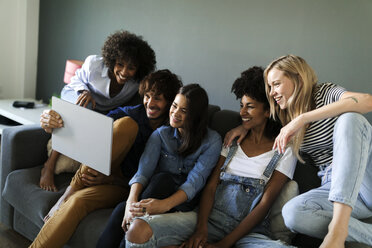 Glückliche Freunde sitzen auf der Couch und schauen auf ein Tablet - VABF01738