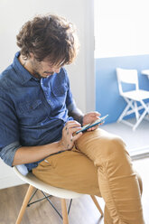 Man sitting on chair at home using cell phone - VABF01758