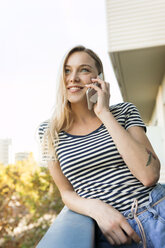 Lächelnde junge Frau, die auf dem Balkon mit einem Handy telefoniert - VABF01760