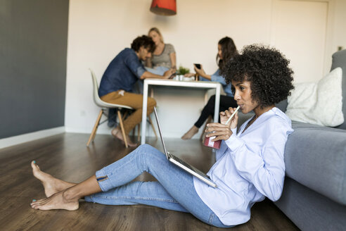 Frau mit Erfrischungsgetränk auf dem Boden sitzend mit Laptop und Freunden im Hintergrund - VABF01769