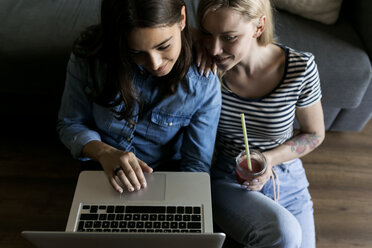 Zwei lächelnde junge Frauen sitzen mit einem Softdrink auf dem Boden und teilen sich einen Laptop - VABF01775