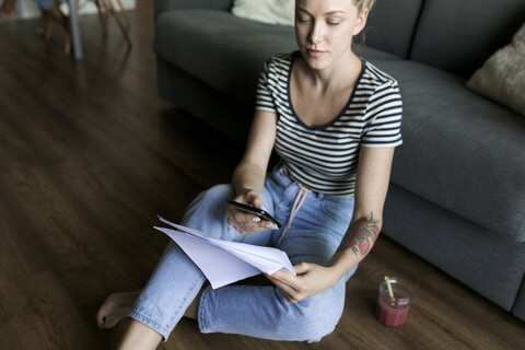 Young woman sitting on floor with cell phone and papers stock photo