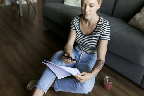 Junge Frau sitzt mit Handy und Papieren auf dem Boden - VABF01782