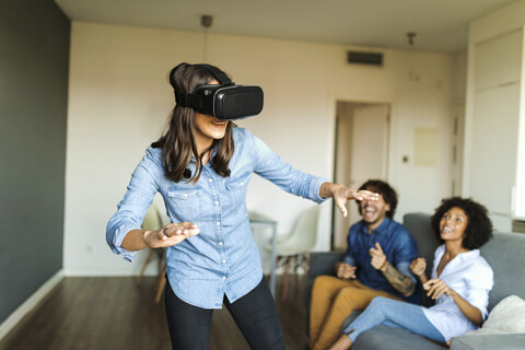Freunde beobachten Frau mit VR-Brille zu Hause, lizenzfreies Stockfoto