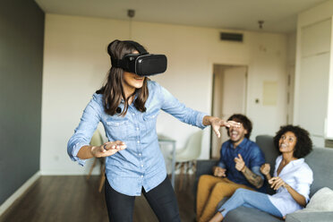 Friends watching woman with VR glasses at home - VABF01789