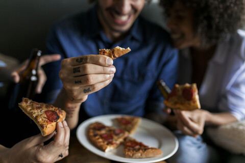 Nahaufnahme eines tätowierten Mannes mit Freunden, der ein Pizzastück hält, lizenzfreies Stockfoto