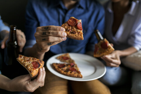 Close-up of tattooed man with friends holding pizza slice stock photo