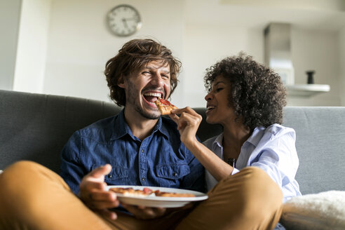 Happy couple sitting on couch eating pizza - VABF01818