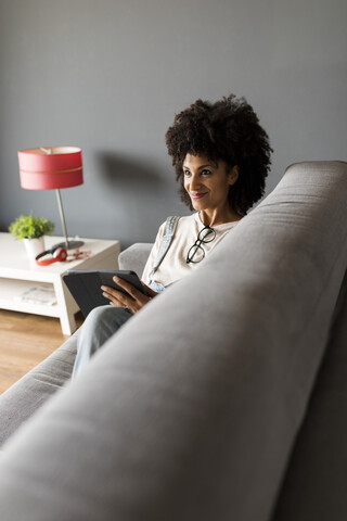 Smiling woman lying on couch at home using tablet stock photo