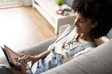 Lächelnde Frau, die zu Hause auf der Couch liegt und ein Tablet benutzt - VABF01826