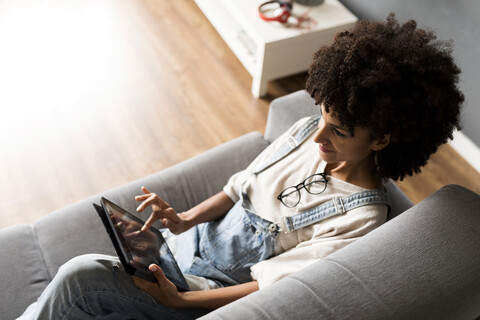 Lächelnde Frau, die zu Hause auf der Couch liegt und ein Tablet benutzt, lizenzfreies Stockfoto