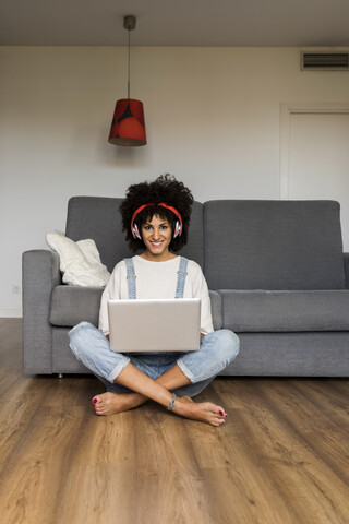 Porträt einer lächelnden Frau, die zu Hause mit Kopfhörern und Laptop sitzt, lizenzfreies Stockfoto