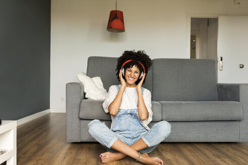 Glückliche Frau sitzt zu Hause mit Kopfhörern - VABF01831