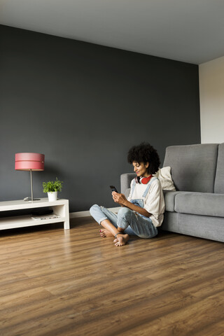 Smiling woman sitting at home with headphones and cell phone stock photo