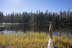 USA, Kalifornien, Yosemite-Nationalpark, Wanderer steht auf einem Baumstamm im Herbst - KKAF03011