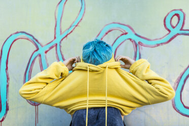 Junge Frau mit gefärbten blauen Haaren, die eine gelbe Kapuzenjacke anzieht - ERRF00109
