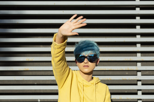 Porträt einer jungen Frau mit blau gefärbtem Haar, die eine verspiegelte Sonnenbrille und eine gelbe Kapuzenjacke trägt - ERRF00111
