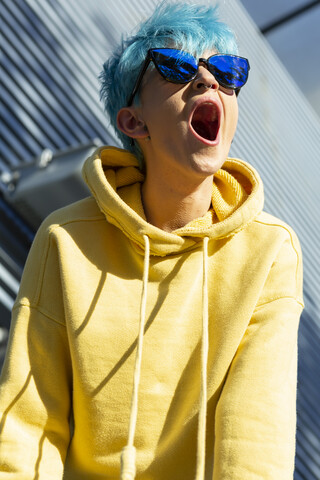 Porträt einer schreienden jungen Frau mit blau gefärbtem Haar und gelber Kapuzenjacke, lizenzfreies Stockfoto