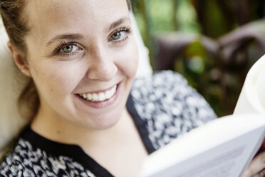 Portrait of happy young woman reading book on balcony - JATF01071