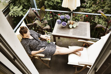 Young woman sitting on balcony with mug of tea using smartphone - JATF01073