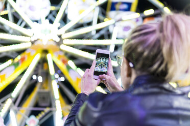 Rückansicht einer Frau, die auf einer Messe mit ihrem Smartphone ein Foto vom Riesenrad macht - FBAF00172