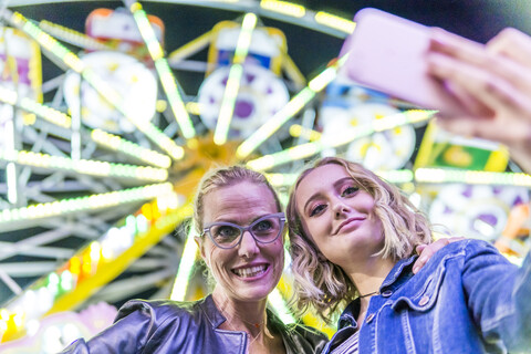 Porträt von Mutter und Tochter, die ein Selfie vor einem Riesenrad auf dem Jahrmarkt machen, lizenzfreies Stockfoto