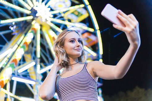 Porträt eines Teenagers, der ein Selfie vor einem Riesenrad auf dem Jahrmarkt macht - FBAF00177