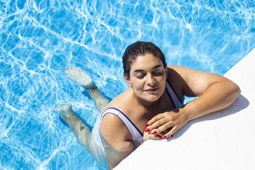 Porträt einer zufriedenen jungen Frau, die sich am Rande eines Swimmingpools entspannt - ERRF00126