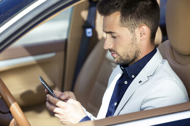 Junger Geschäftsmann sitzt im Auto und benutzt sein Smartphone - JSRF00073